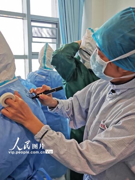 2月22日，武汉华中科技大学同济医学院附属同济医院中法新城院区，北京医院国家医疗队负责的病区。医护人员在防护服上写下姓名，整装待发。（陈黎明 人民图片）